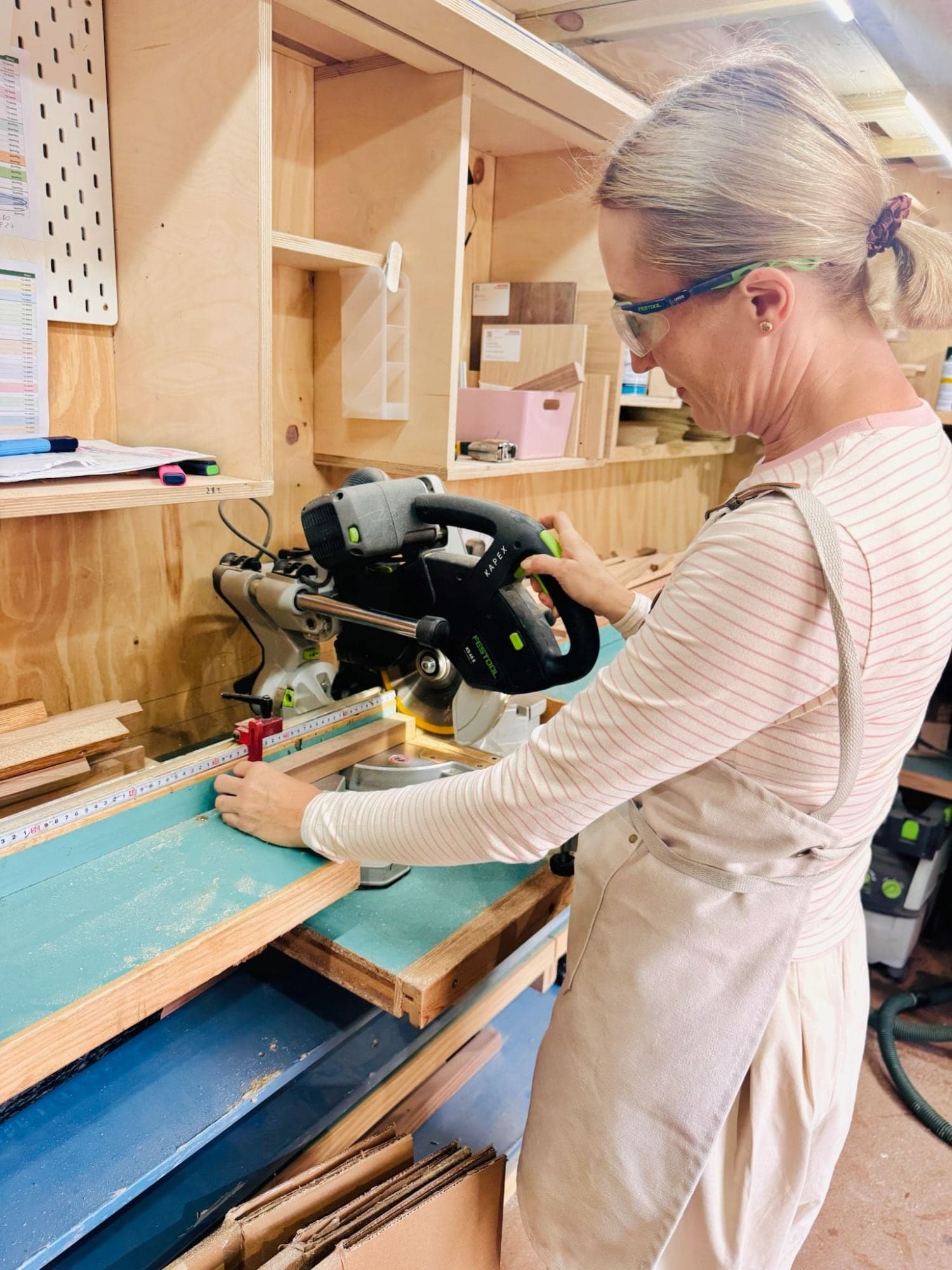 Kat cutting a length of wood on the mitre saw, wearing safety glasses